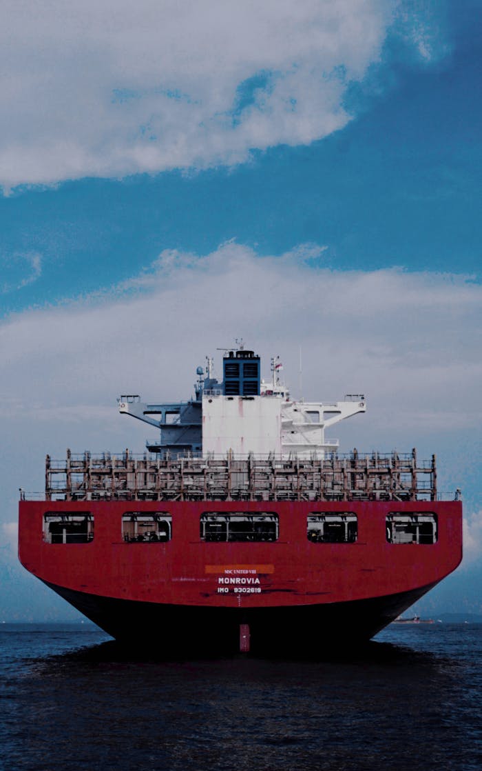 Large red cargo ship transporting goods across the ocean under a bright blue sky.